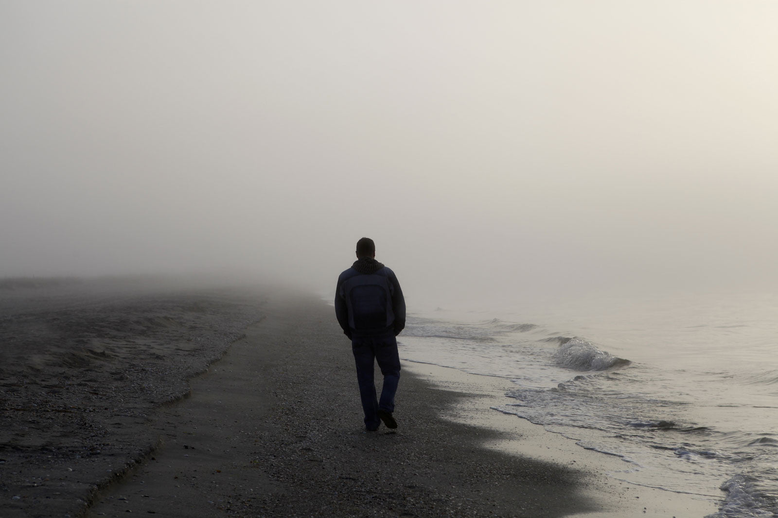 Man walking alone on grey, dreary beach