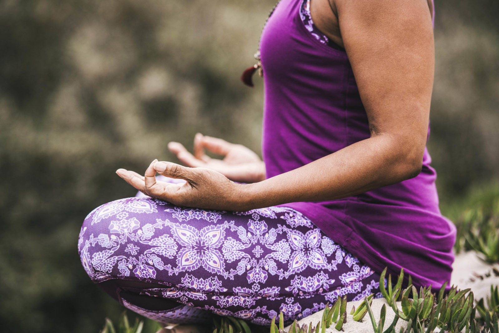 Woman sitting in meditation outside in purple yoga clothes