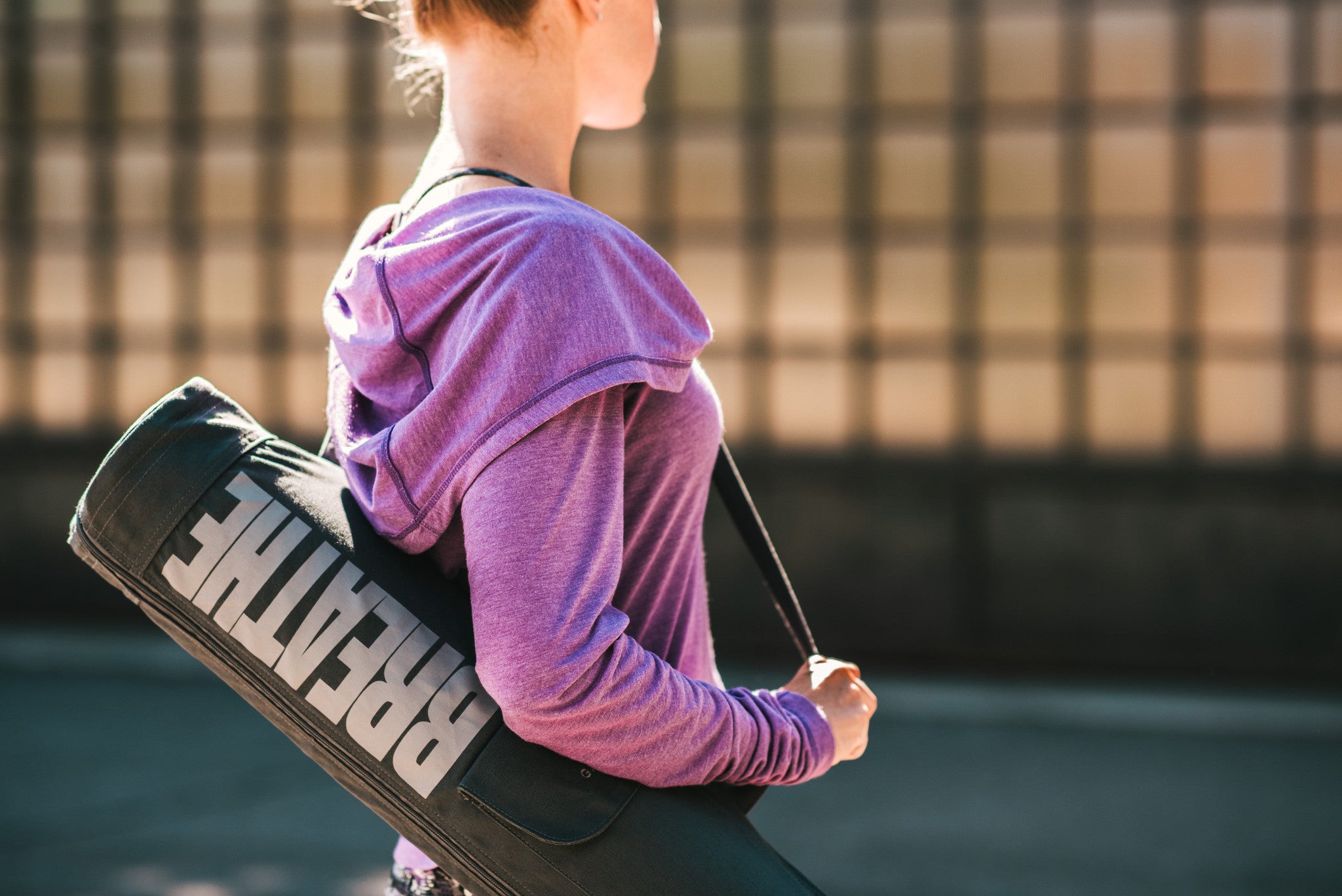 Woman holds yoga mat bag saying breathe on her shoulder