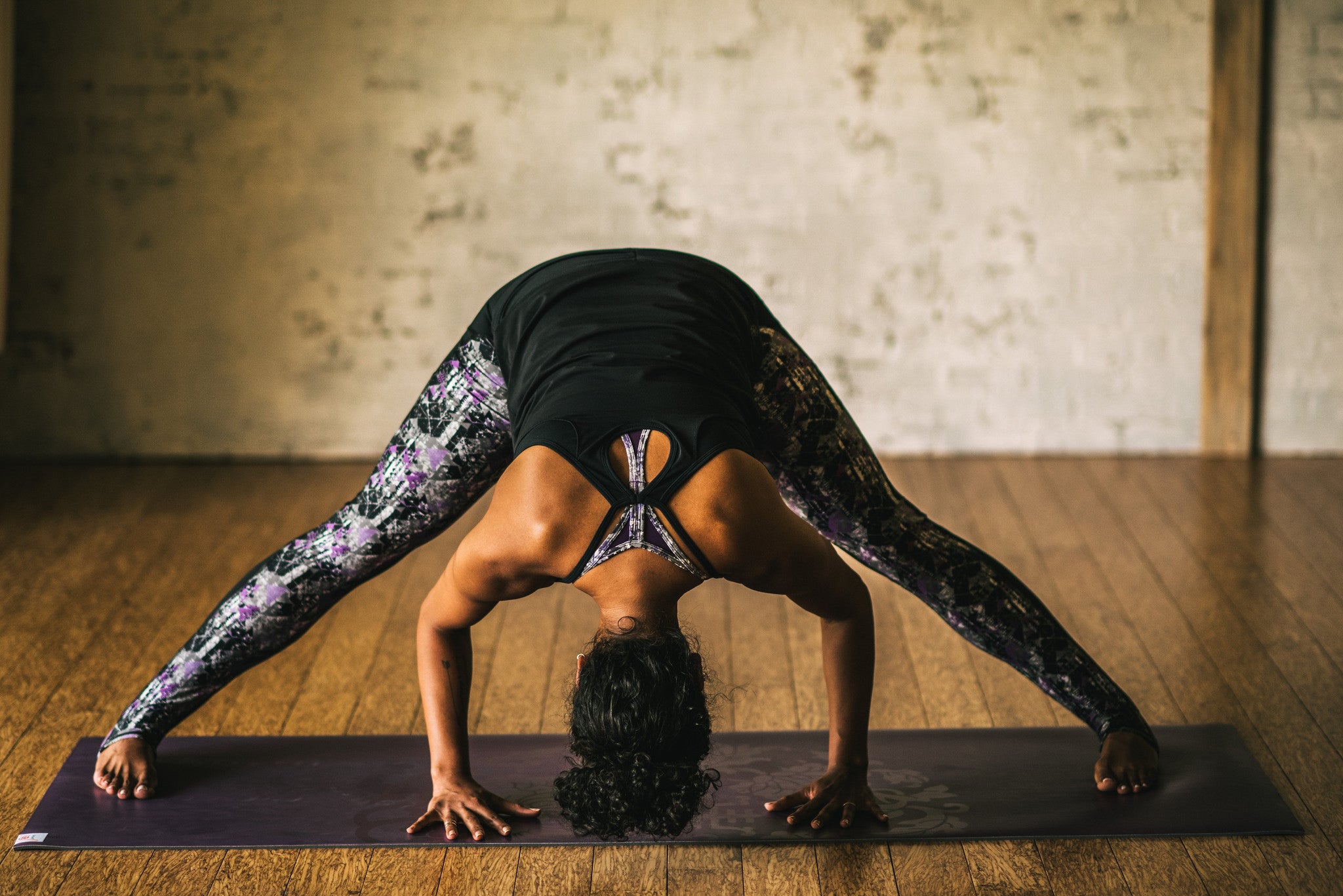 Woman in yoga outfit does wide legged forward fold on yoga mat