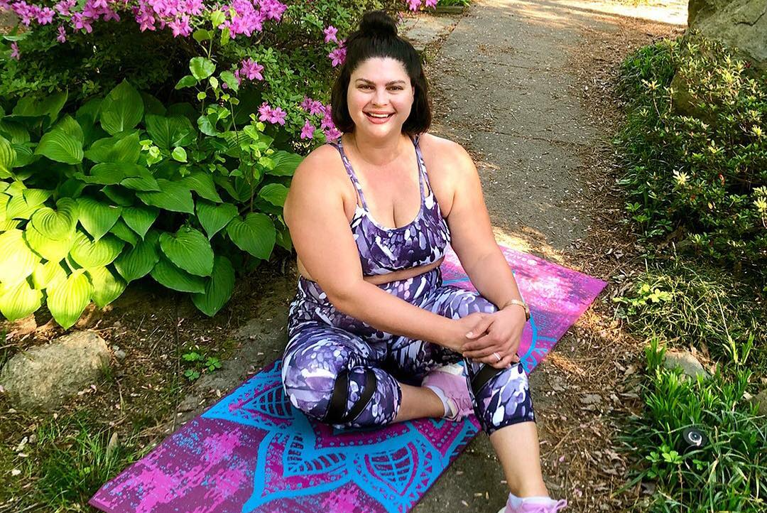 woman sits on colorful yoga mat in front of flowers