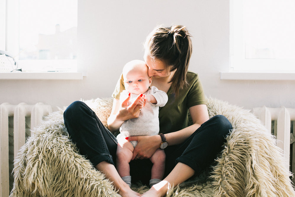 young mom with dark hair in a pony tail holds her new baby on a fur chair