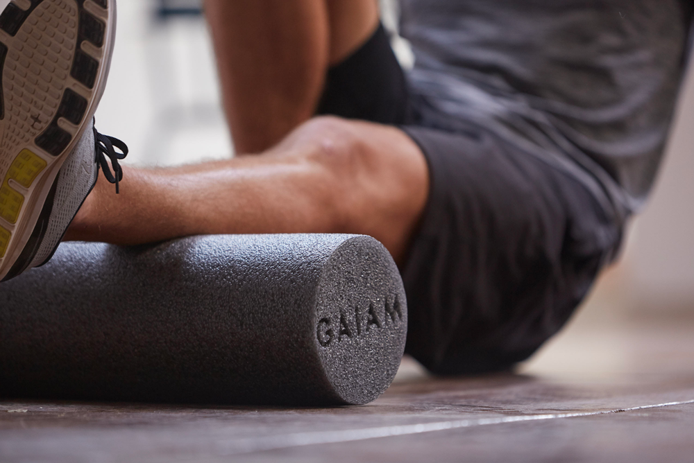man uses grey foam roller on calf