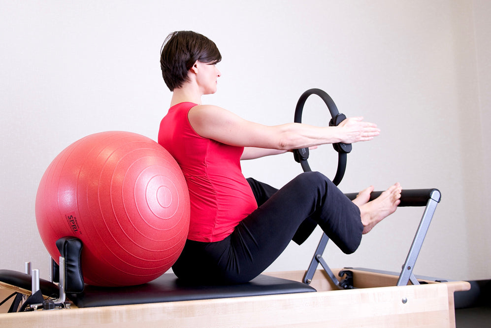 pregnant woman uses pilates ring and balance ball on a reformer