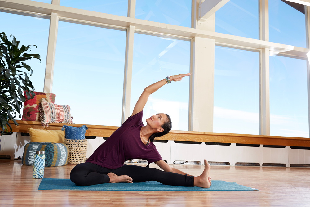 woman stretches on yoga mat in front of big window