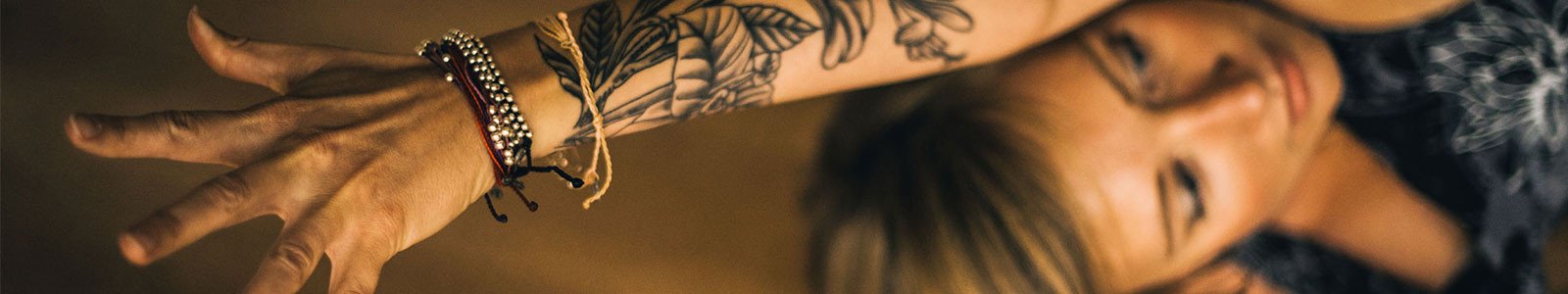 Woman with tattoos and bracelets extending her arm overhead.