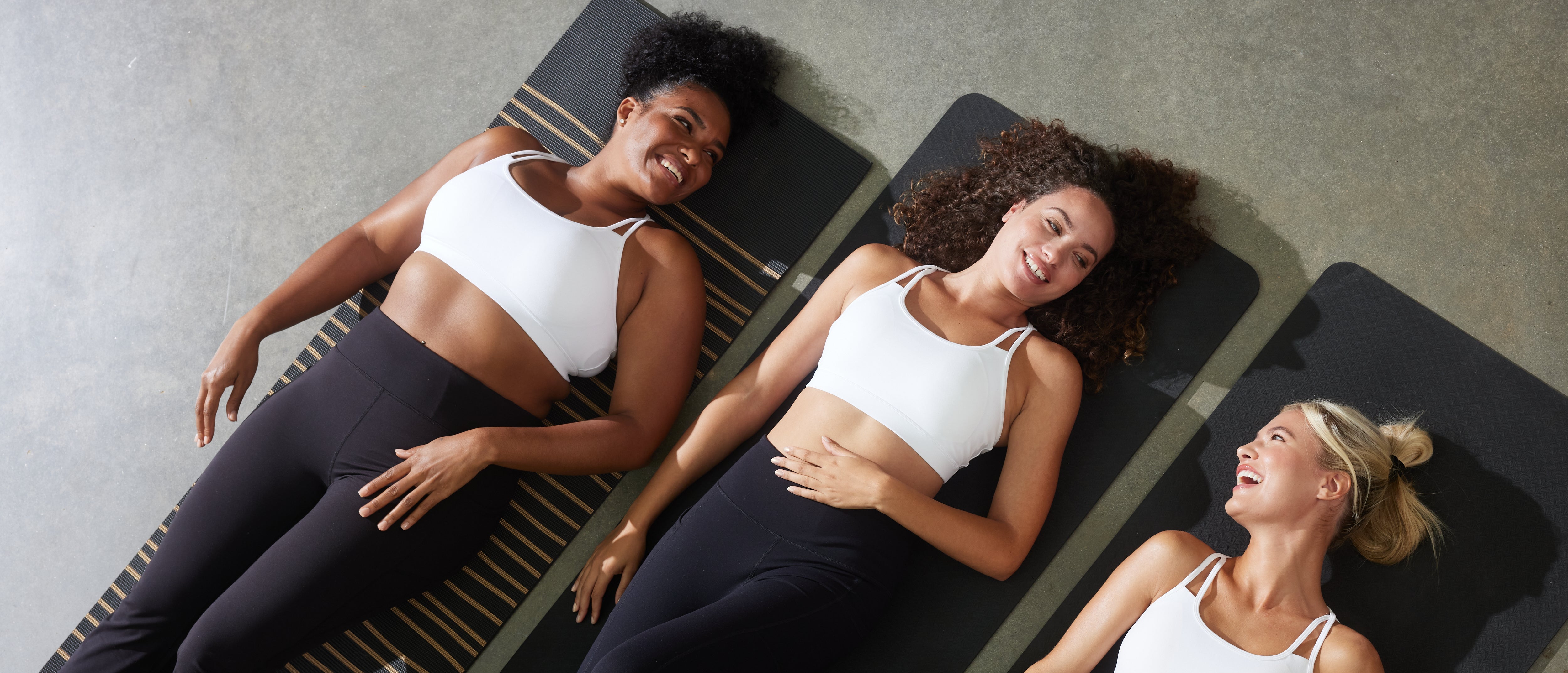 Three women lying on exercise mats in a studio setting