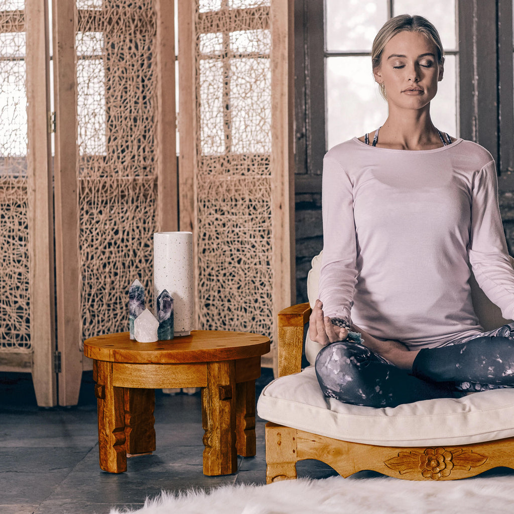 honey brown table next to woman meditating in raja chair