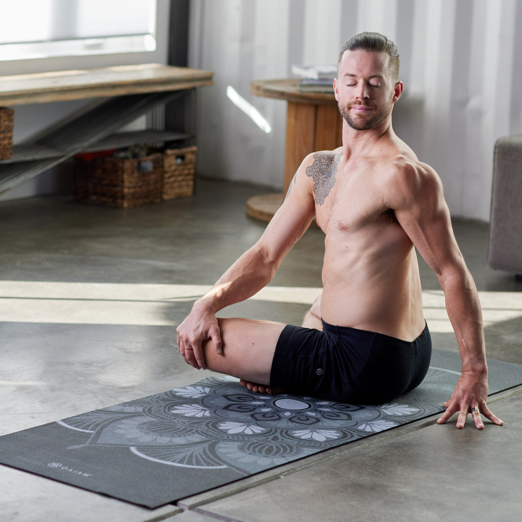 Person sitting on Yoga Mat with crossed legs, twisting to the side with eyes closed