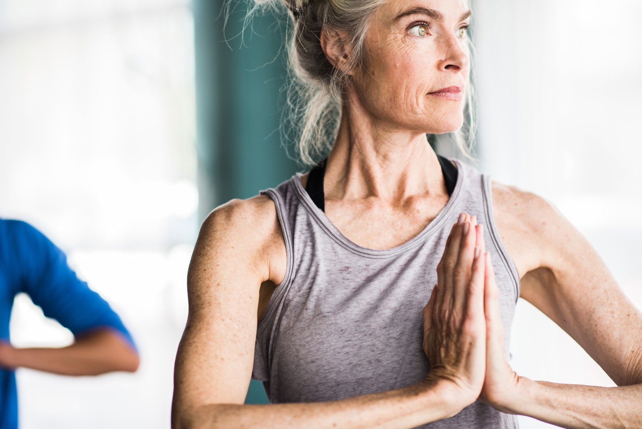 Older woman does twisting prayer yoga pose in grey tank top