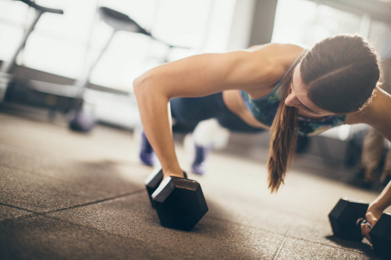 Woman doing push-up on dumbbells 