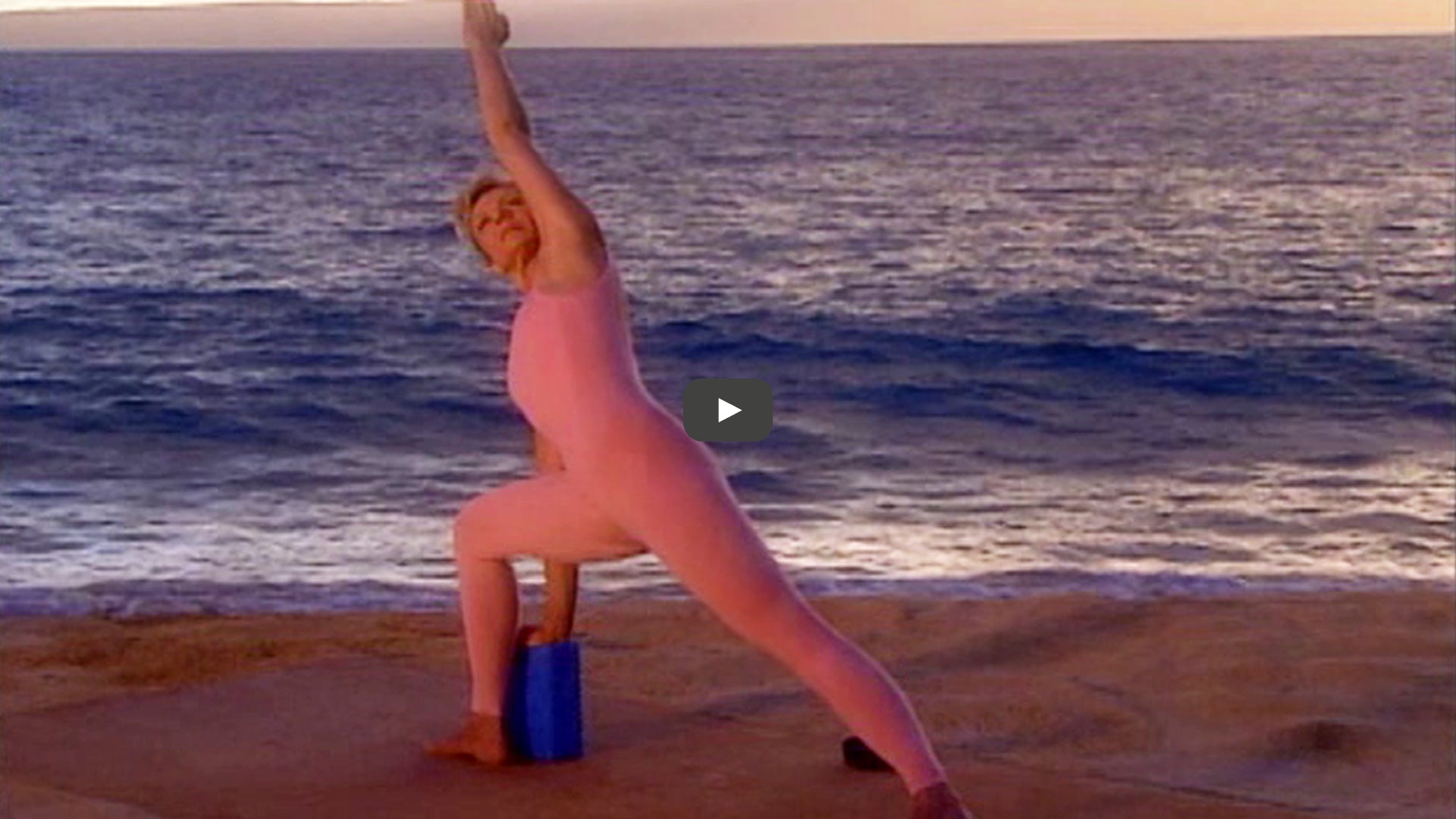 woman does extended side angle with block on beach