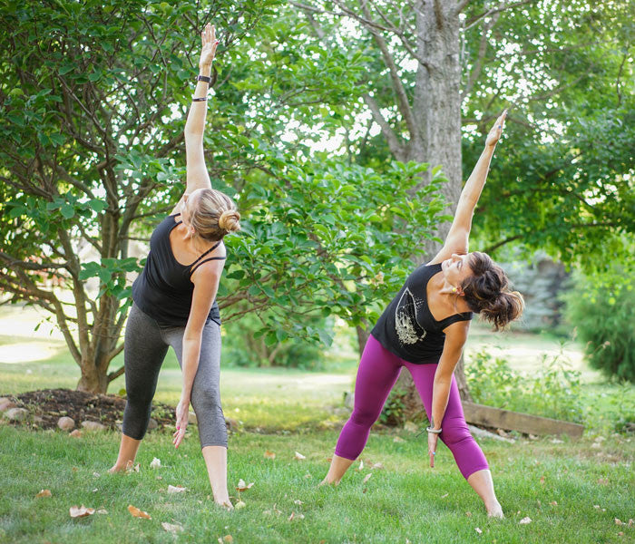 two women do triangle pose in a park