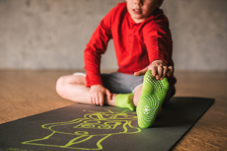 Young boy in a red shirt and green socks stretches on yoga mat
