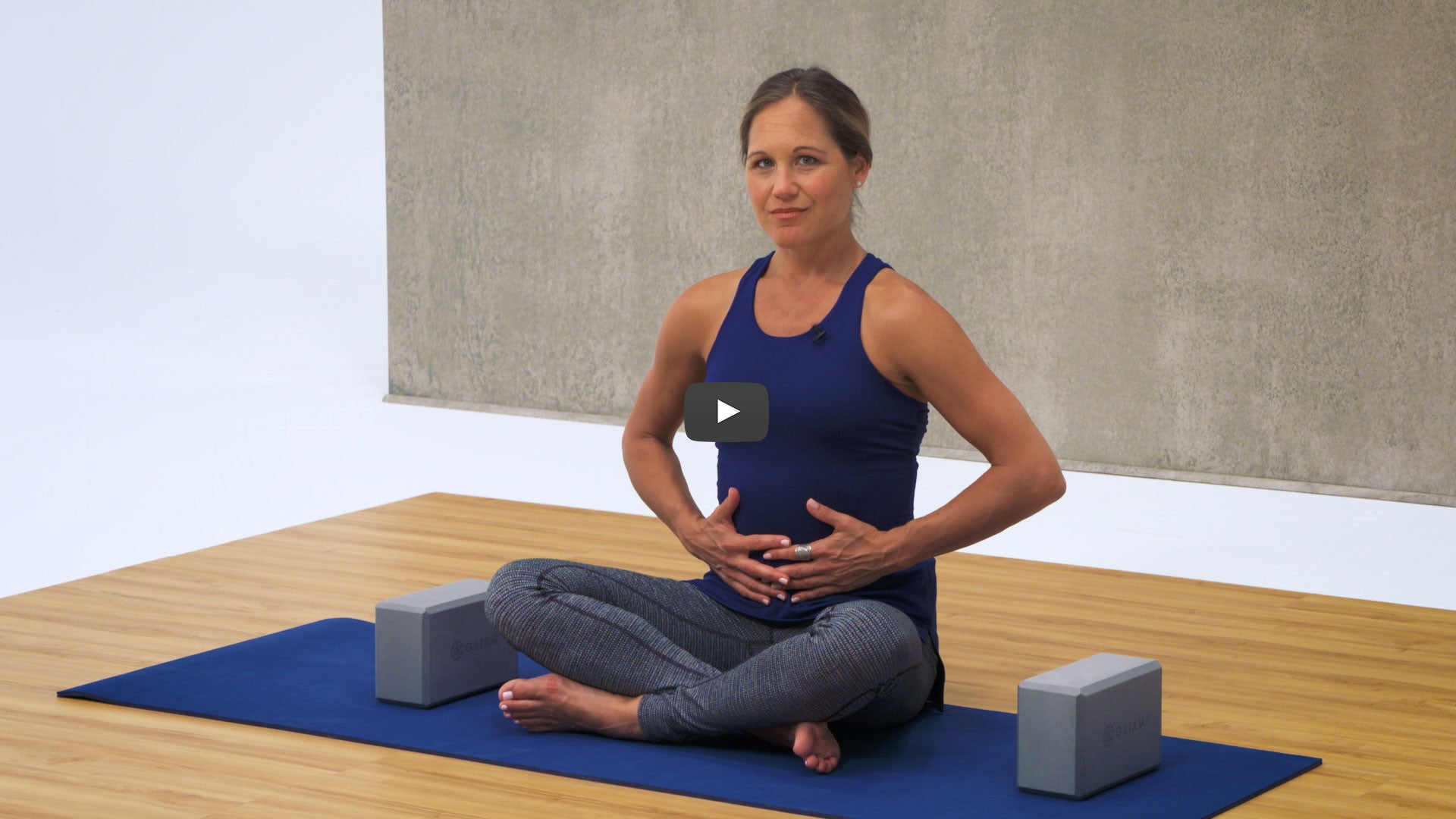Woman sits on yoga mat holding stomach