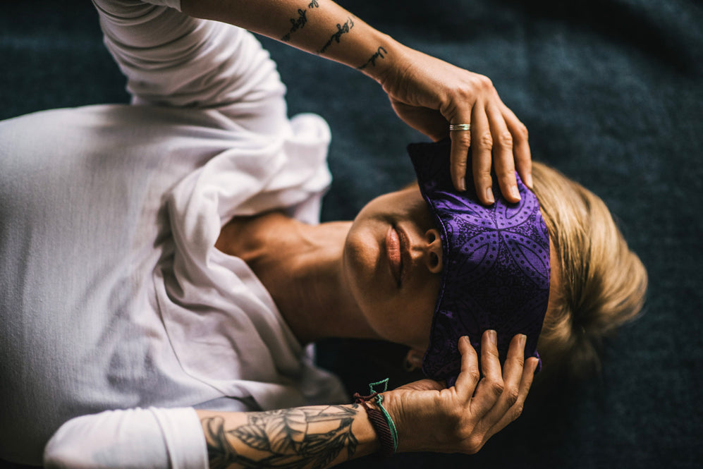 A blonde-haired woman lays on floor with eye pillow