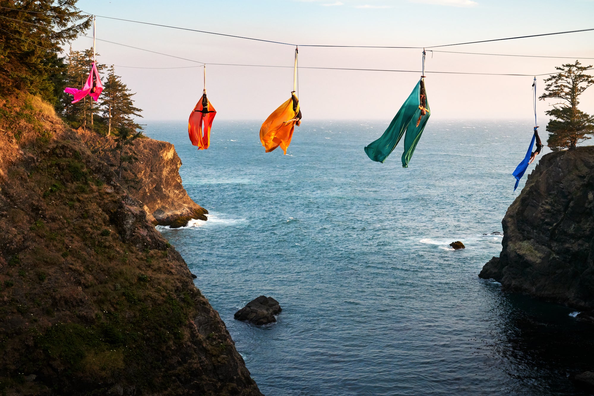 Rainbow colored aerial silks hang over the Pacific Ocean