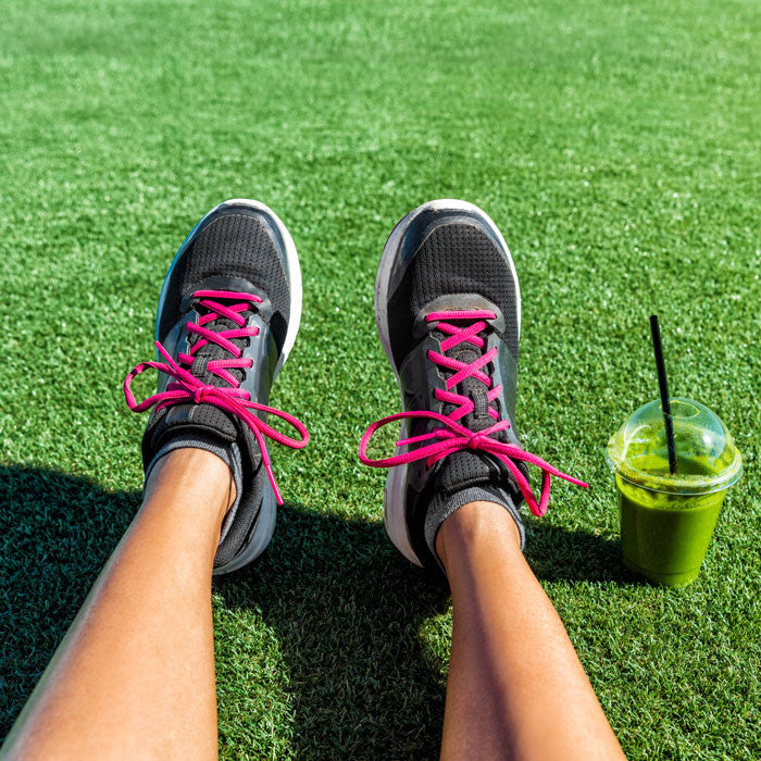 Person wearing sneakers outside with green smoothie