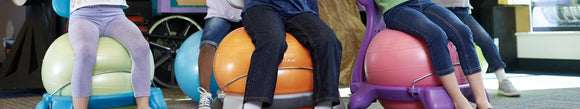 A group of kids sitting on different colored balance ball chairs.