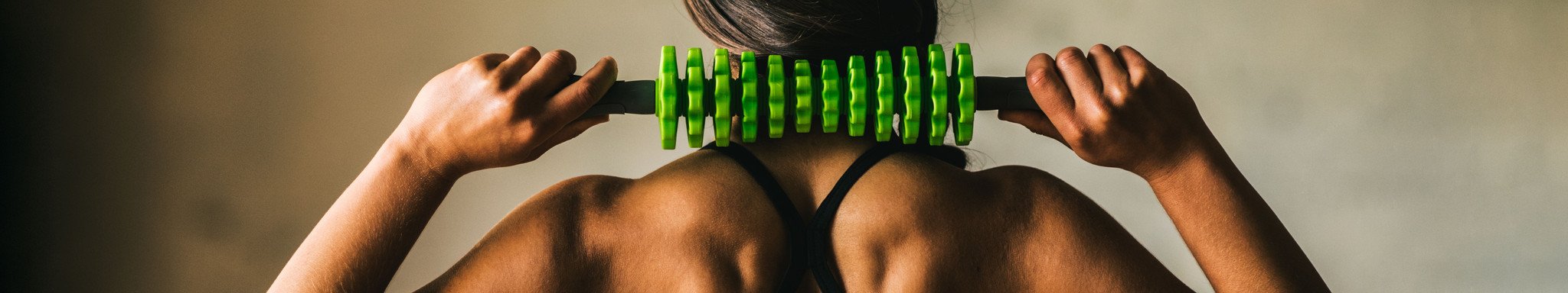 Strong woman massaging back of neck with green adjustable massage roller.